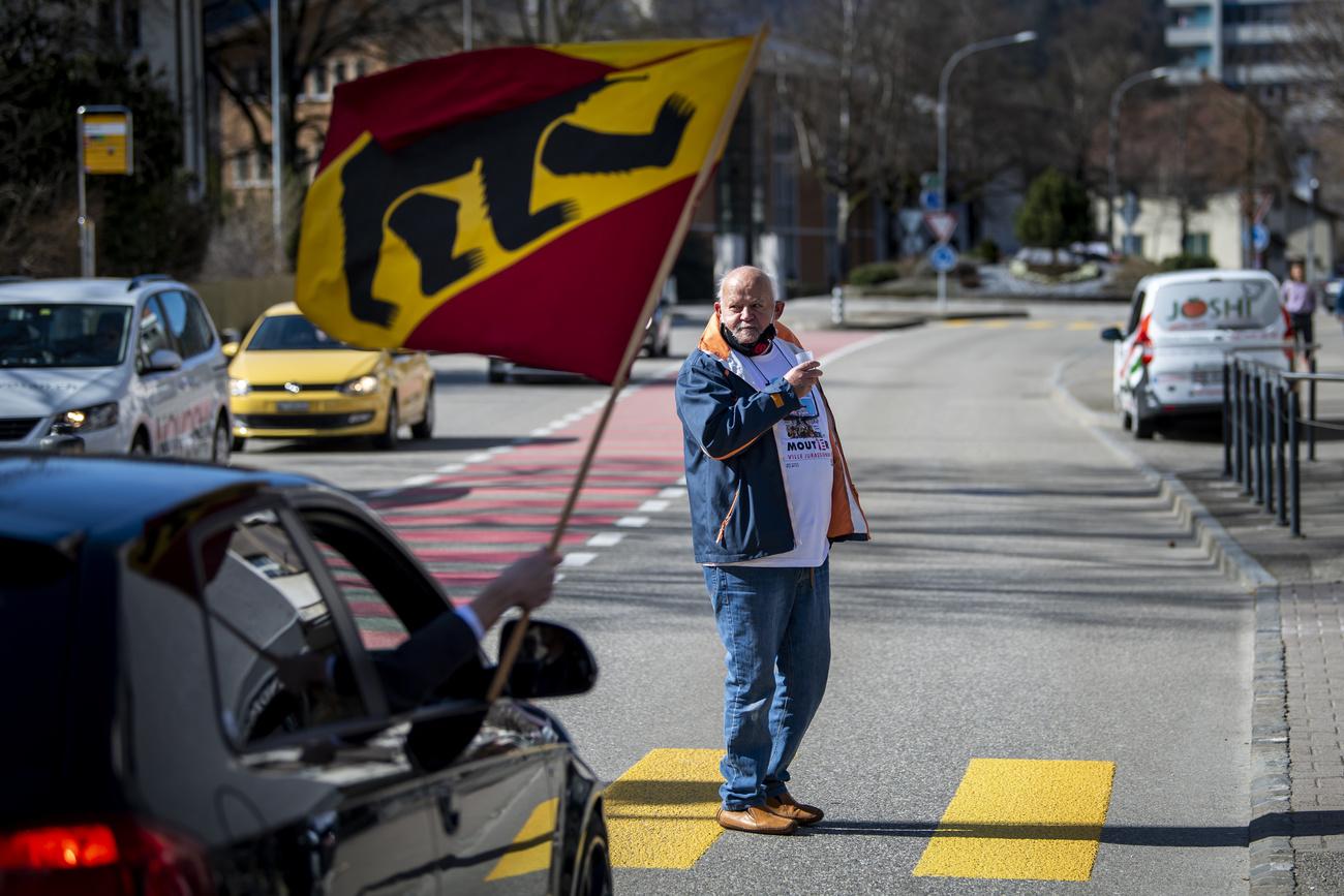 Les drapeaux des deux camps commencent à sortir à Moutier. Une voiture avec un militant pro-bernois passe devant un homme portant un t-shirt pro-jurassien. [Keystone - Jean-Christophe Bott]