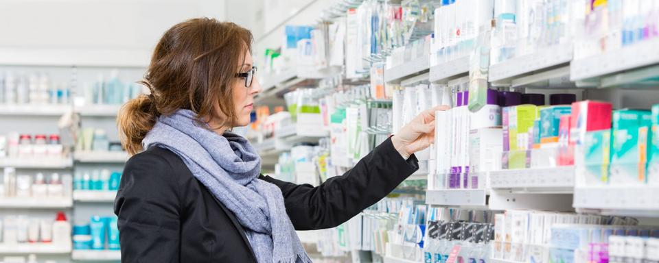 Une femme examine un produit dans les rayons d'une pharmacie. [Depositphotos - SimpleFoto]