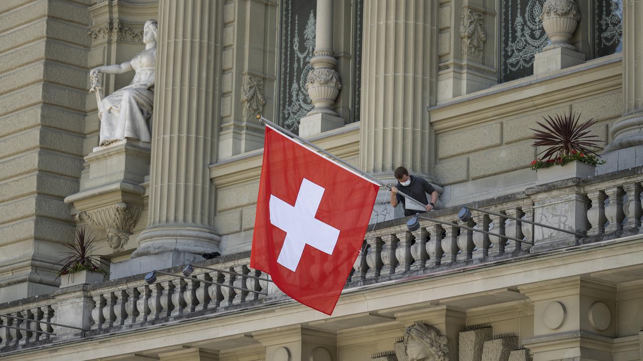 Un collaborateur du Parlement fédéral accroche un drapeau au balcon du Palais fédéral au début de de la session d'été le 31 mai 2021. [Keystone - Alessandro della Valle]