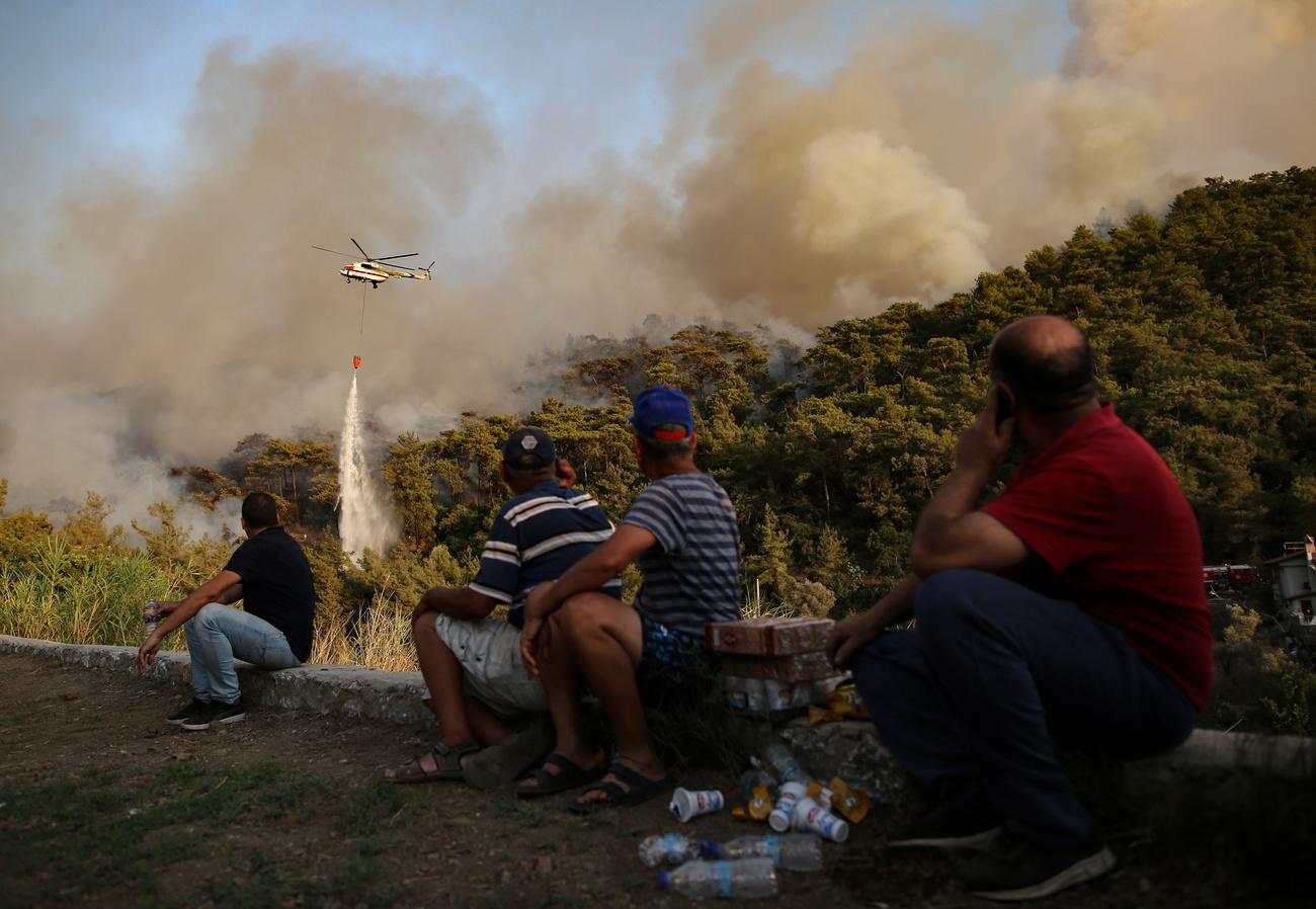 Des habitants d'une zone rurale de Marmaris observent un hélicoptère bombardier d'eau en action. [Keystone/EPA - Erdem Sahin]