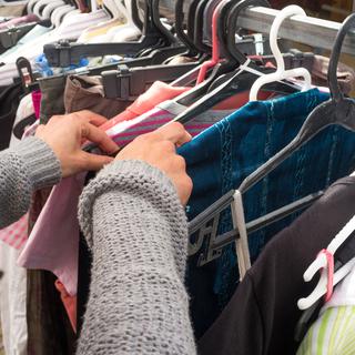 Femme regardant des vêtements dans une boutique de seconde main. [Depositphotos - OlafSpeier]