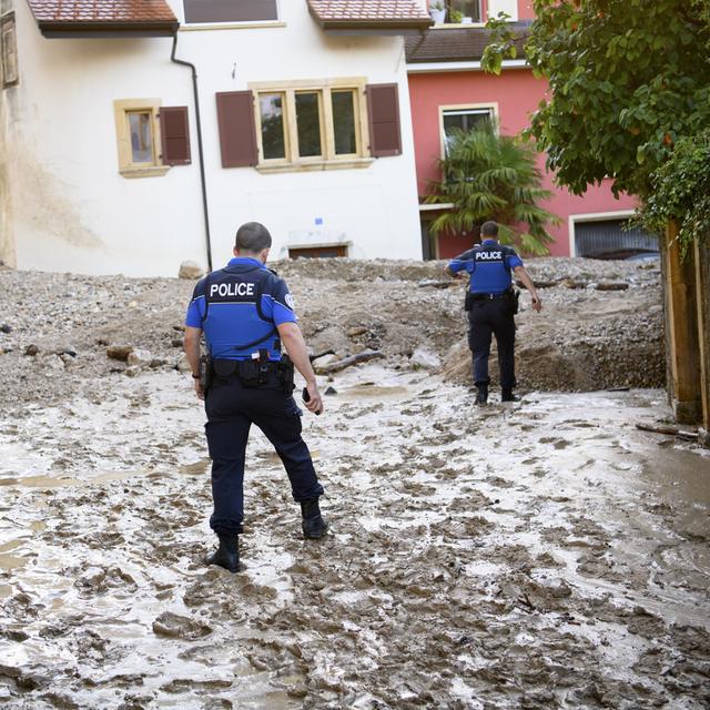 Des policiers dans la rue recouverte du boue à Cressier. [Keystone - Laurent Gillieron]