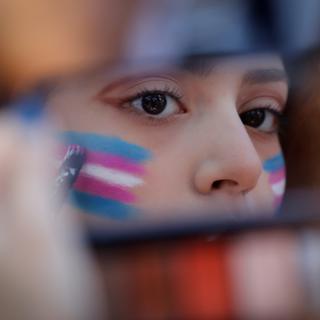 Une personne se peint le drapeau de la communauté transgenre sur le visage. [Keystone/epa - Francisco Guasco]