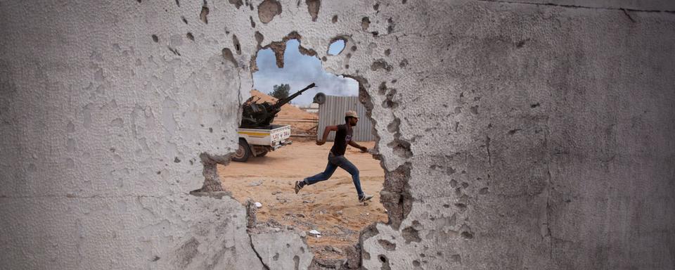 Un combattant révolutionnaire libyen court se mettre à l'abri durant l'attaque de forces pro-Kadhafi à Syrte, en Libye, le 7 octobre 2011. Les forces rebelles assiégeaient alors Syrte depuis le 15 septembre sans réussir à pénétrer au cœur de la ville en raison de la résistance acharnée des loyalistes du dirigeant libyen Muammar Kadhafi. La guerre civile de 2011 en Libye, également connue sous le nom de Révolution du 17 février, a éclaté cette année-là dans le sillage du Printemps arabe. [Keystone/AP - Manu Brabo]