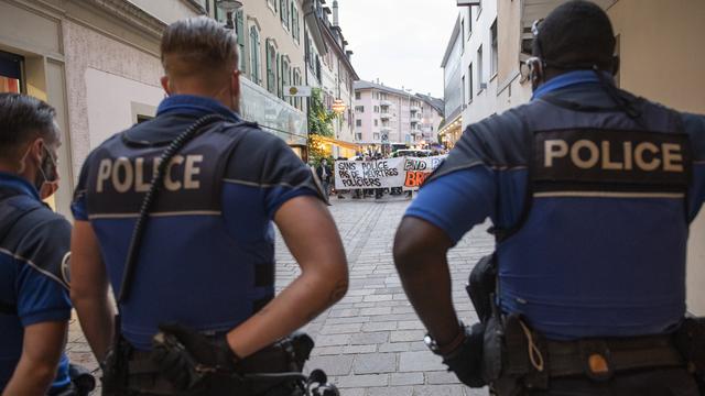 Trois policiers sont vus de dos et font face à la manifestation contre les violences policières à Morges. [Keystone - Jean-Guy Python]