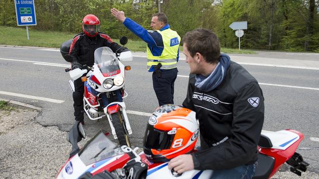 Un gendarme de la brigade de prévention routière de la Police cantonale vaudoise arrête un motard, sous les yeux du pilote motocycliste Bastien Chesaux, lors d'une action de prévention en 2014 sur la route Blanche entre Nyon et Saint-Cergue. [Keystone - Jean-Christophe Bott]