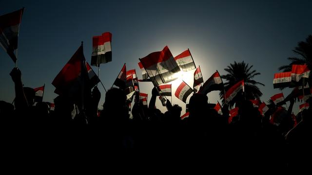 À contre-jour, des bras tendus brandissent des drapeaux irakiens. [AP Photo/Keystone - Hadi Mizban]