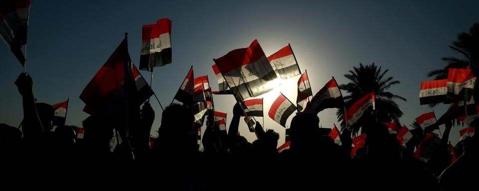 À contre-jour, des bras tendus brandissent des drapeaux irakiens. [AP Photo/Keystone - Hadi Mizban]