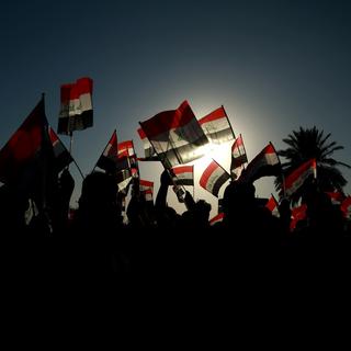 À contre-jour, des bras tendus brandissent des drapeaux irakiens. [AP Photo/Keystone - Hadi Mizban]