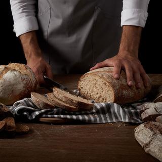 Gros plan sur des mains coupant du pain. [Depositphotos - AntonMatyukha]