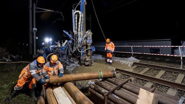 Des ouvriers font un forage pour préparer le terrain à l'emplacement du trou sur la ligne CFF entre Lausanne et Genève suite à un affaissement survenu en bordure de voie à Tolochenaz (VD). [Keystone - Jean-Christophe Bott]