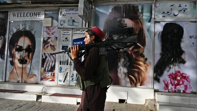 Un combattant taliban passe devant un salon de beauté avec des images de femmes recouvertes de peinture, à Kaboul, le 18 août 2021. [AFP - Wakil Kohsar]