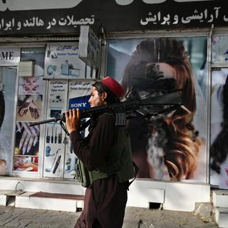 Un combattant taliban passe devant un salon de beauté avec des images de femmes recouvertes de peinture, à Kaboul, le 18 août 2021. [AFP - Wakil Kohsar]