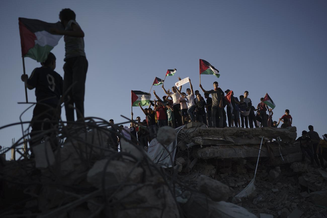 Des personnes brandissent des drapeaux palestiniens, du haut des gravats d'un immeuble détruit par une frappe israélienne le mois dernier, en protestation contre la "marche des drapeaux". Beit Lahia, Gaza, le 15 juin 2021. [Keystone/AP photo - Felipe Dana]