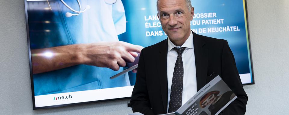 Le conseiller d'Etat neuchatelois Laurent Kurth consulte une brochure sur "Mon Dossier Santé". [Keystone - Jean-Christophe Bott]