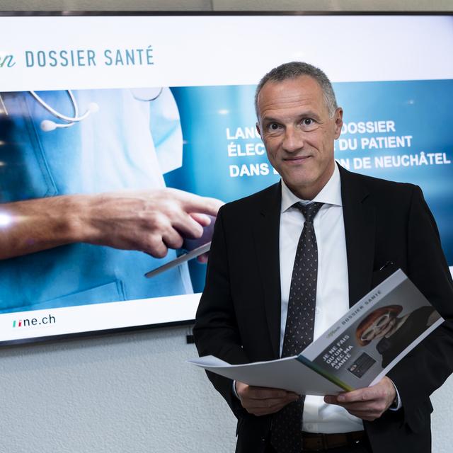 Le conseiller d'Etat neuchatelois Laurent Kurth consulte une brochure sur "Mon Dossier Santé". [Keystone - Jean-Christophe Bott]