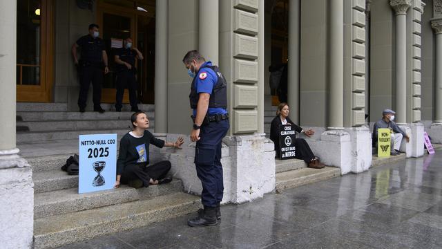 Un policier parle avec des militants d'Extinction Rebellion qui se sont collés la main à la glu sur le Palais fédéral à Berne. [Keystone - Anthony Anex]