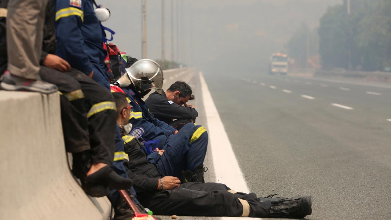 Vendredi 6 août: épuisés par une interminable lutte contre les incendies, des pompiers reprennent haleine sur le bas-côté de l'autoroute Athènes-Lamia. [Keystone/EPA - Alexander Beltes]