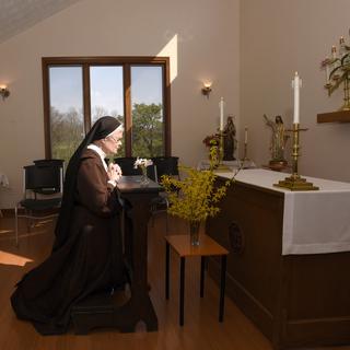 The Rev. Sister Barbara Smith, of the Order of Discalced Carmelites, prays on a prayer bench that belonged to The Rev. Mychal Judge, the Fire Department of New York's chaplain who died in the 2001 attacks on the World Trade Center, at the Episcopal Carmel of Saint Teresa in Rising Sun, Md., on Sunday, April 4, 2021. The Episcopal Carmel of Saint Teresa donated the prayer bench to the National Sept. 11 Memorial and Museum, representatives of which acquired the bench later in the morning. (AP Photo/Steve Ruark) [Keystone/ AP - Steve Ruark]