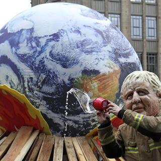 Un militant d'Oxfam déguisé en Boris Johnson, le Premier ministre britannique, dans le rôle des "leaders mondiaux inefficaces qui luttent contre le feu", pose pour une photo lors d'une rencontre avec la presse à proximité du Sommet des Nations Unies sur le climat COP26 à Glasgow, en Écosse, vendredi 12 novembre 2021. [AP Photo/Keystone - Scott Heppell]