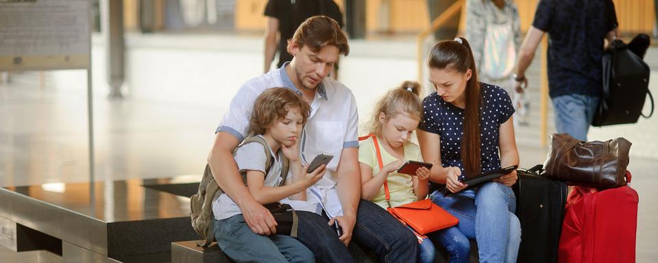 Une famille regarde les billets de train en ligne assis dans une gare. [Depositphotos - unguryanu]