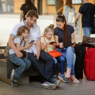 Une famille regarde les billets de train en ligne assis dans une gare. [Depositphotos - unguryanu]