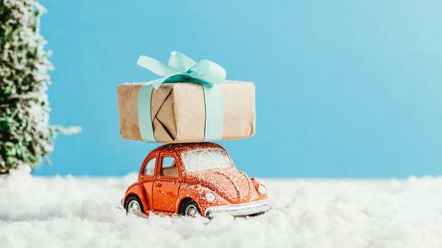 Une petite voiture transporte un cadeau sur son toit. [Depositphotos - EdZbarzhyvetsky]