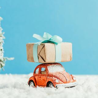 Une petite voiture transporte un cadeau sur son toit. [Depositphotos - EdZbarzhyvetsky]