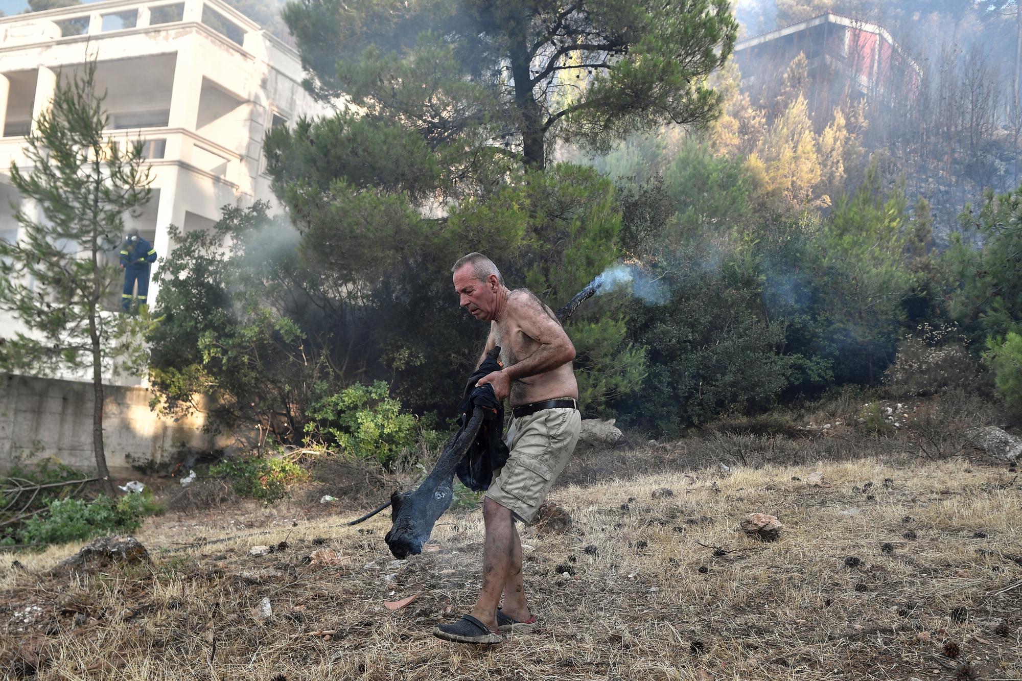 Les habitants sont à pied d'oeuvre pour lutter contre les incendies en Grèce. Ici, un homme déplace une branche d'arbre incandescente pour éviter une reprise des flammes. [AFP - Louisa Gouliamaki]