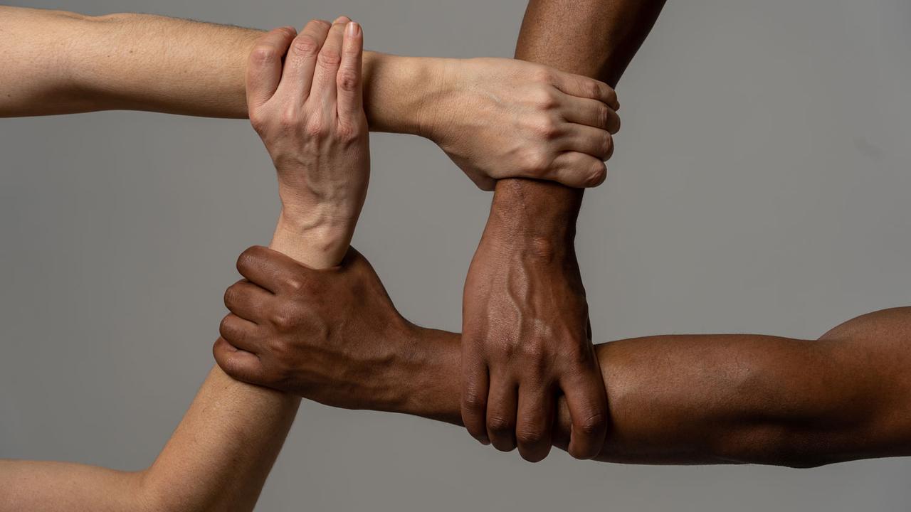 Quatre personnes de couleur de peau différente se tiennent la main. [Depositphotos - samwordley@gmail.com]