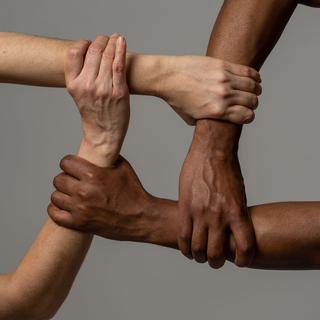 Quatre personnes de couleur de peau différente se tiennent la main. [Depositphotos - samwordley@gmail.com]