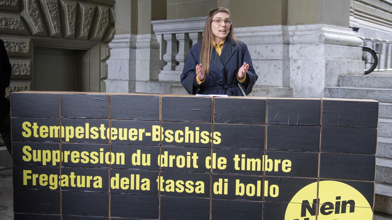 Franziska Ryser se tient derrière une banderole sur laquelle est écrit dans les trois langues nationales: "Suppression du droit de timbre". [Keystone - Marcel Bieri]