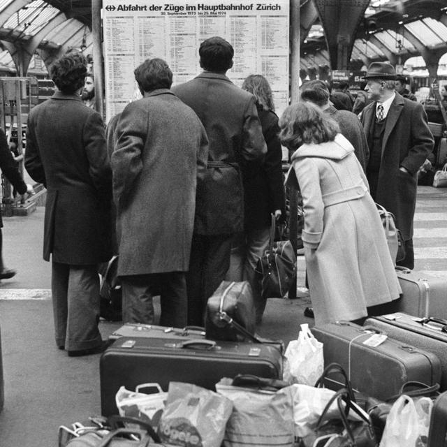Des travailleurs immigrés consultent l'horaire des trains en gare de Zurich le 16 décembre 1973. De nombreux travailleurs étrangers profitent de leurs jours de congé pour rendre visite à leur famille restée au pays. [KEYSTONE/PHOTOPRESS-ARCHIV]
