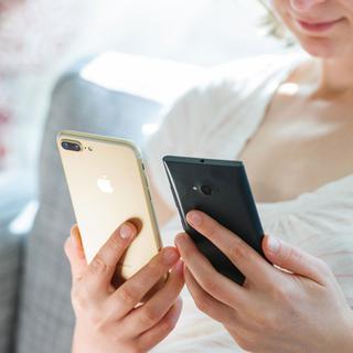 Gros plan sur les mains d'une femme tenant deux smartphones de différentes marques. [Depositphotos - ifeelstock]