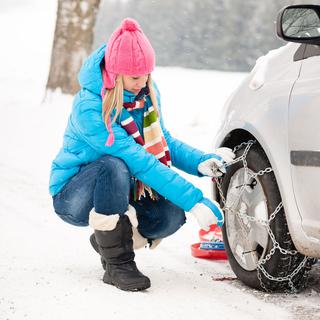 Une femme met les chaînes à neige sur sa voiture. [Depositphotos - CandyBoxImages]