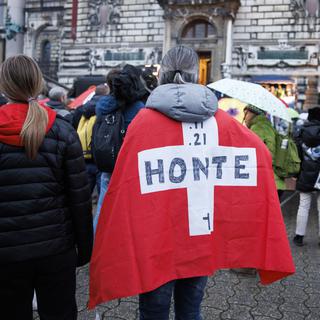 Une femme portant un drapeau suisse sur le dos avec écrit "honte" au stylo noir. [Keystone - Cyril Zingaro]