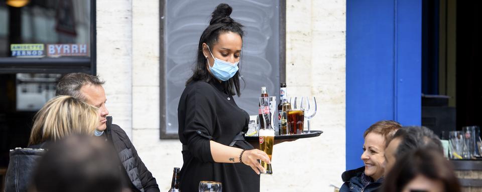 Une serveuse amène des boissons à une table en portant un masque. [KEYSTONE - Laurent Gillieron]