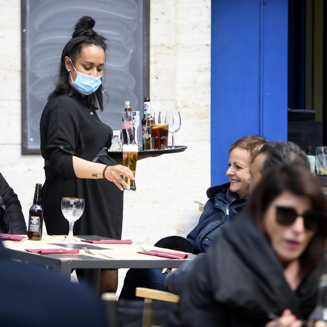 Une serveuse amène des boissons à une table en portant un masque. [KEYSTONE - Laurent Gillieron]