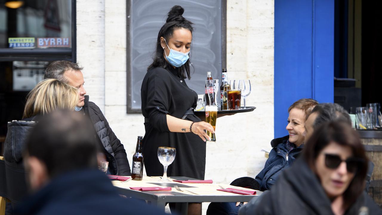 Une serveuse amène des boissons à une table en portant un masque. [KEYSTONE - Laurent Gillieron]