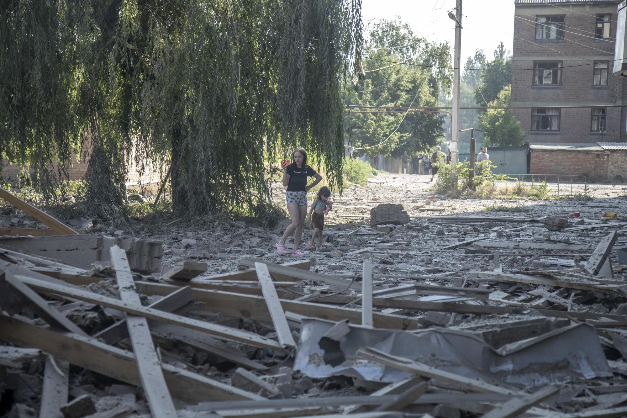 Une mère et sa fille au milieu des débris laissés par l'explosion d'un missile dans la ville de Bakhmut, dans la région de Donetsk, le 6 juillet 2022. [AFP - Narciso Contreras]