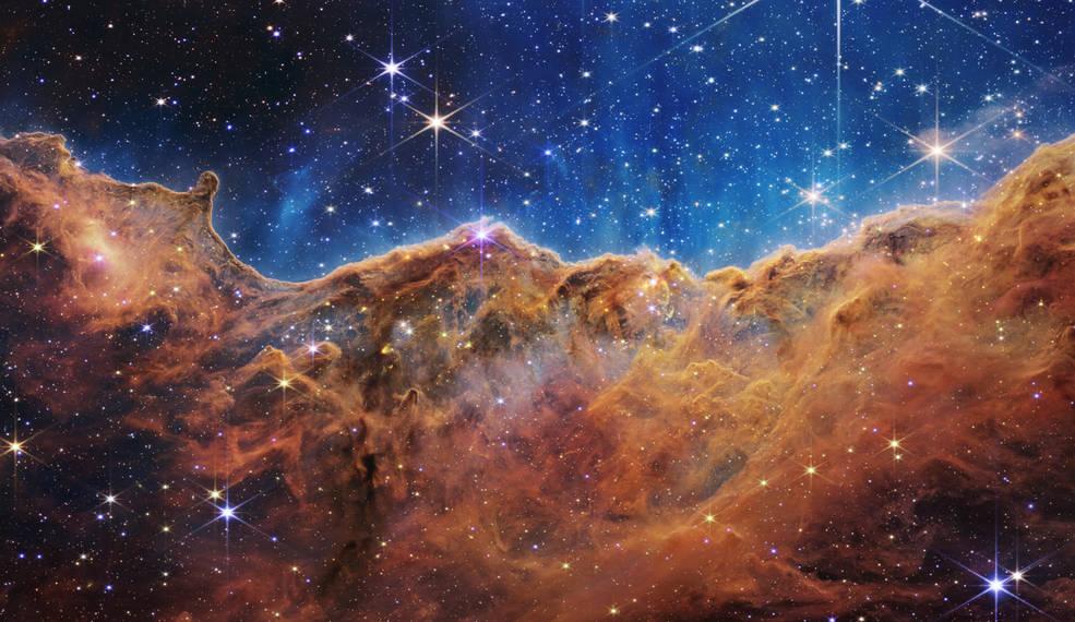 Ce paysage de "montagnes" et de "vallées" parsemées d'étoiles scintillantes est le bord d'une jeune région de formation d'étoiles à proximité appelée NGC-3324 dans la Nébuleuse de la Carène. Capturée en lumière infrarouge par le télescope spatial James Webb, cette image révèle pour la première fois des zones de naissance d'étoiles auparavant invisibles. [NASA, ESA, CSA, and STScI]