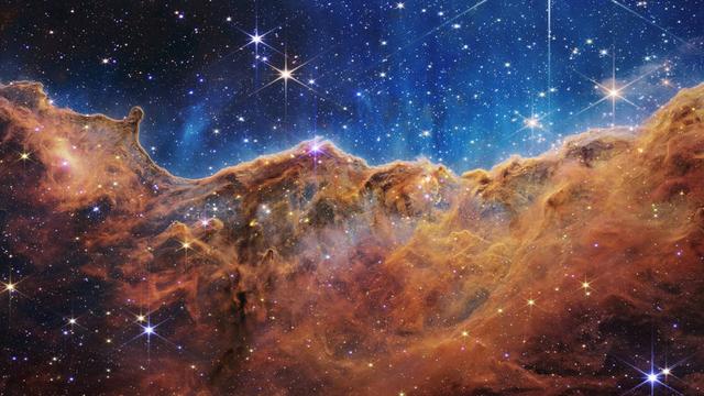 Ce paysage de "montagnes" et de "vallées" parsemées d'étoiles scintillantes est le bord d'une jeune région de formation d'étoiles à proximité appelée NGC-3324 dans la Nébuleuse de la Carène. Capturée en lumière infrarouge par le télescope spatial James Webb, cette image révèle pour la première fois des zones de naissance d'étoiles auparavant invisibles. [NASA, ESA, CSA, and STScI]