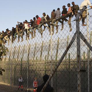 Des migrants sont assis au sommet d'une clôture alors qu'ils tentent de rejoindre Melilla, l'exclave espagnole sur la côte nord-africaine, le 22 octobre 2014. [EPA/KEYSTONE - Francisco G. Guerrero]