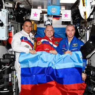 Les cosmonautes russes Sergei Korsakov, Oleg Artemyev et Denis Matveyev posent avec un drapeau de la République populaire autoproclamée de Lougansk à bord de la Station spatiale internationale (ISS). [AFP - Roscosmos]