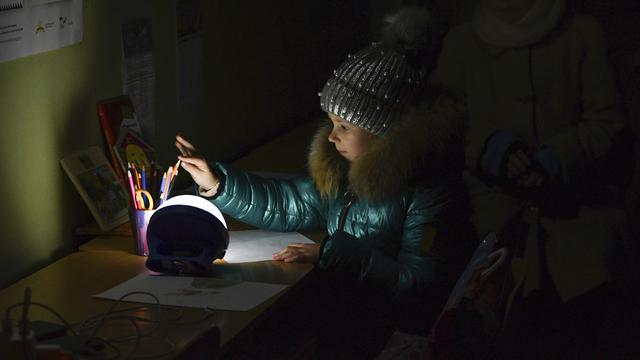 Une petite fille dessins à la lumière d'une lampe alimentée par une génératrice, dans une école alimenté par le gouvernement. [AP/Keystone - Andriy Andriyenko]