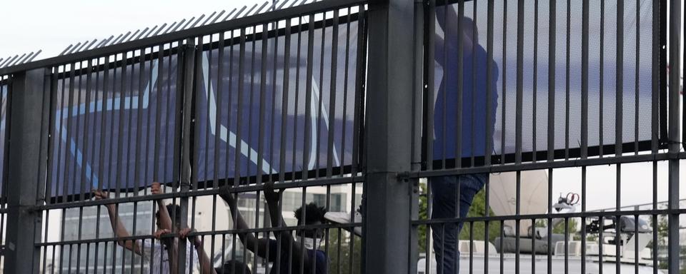 Des supporters ont tenté d'escalader les barrières pour entrer dans le stade. [Keystone/AP - Christophe Ena]