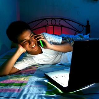 Un adolescent discute au téléphone tout en regardant son ordinateur. [Depositphotos - Junpinzon]