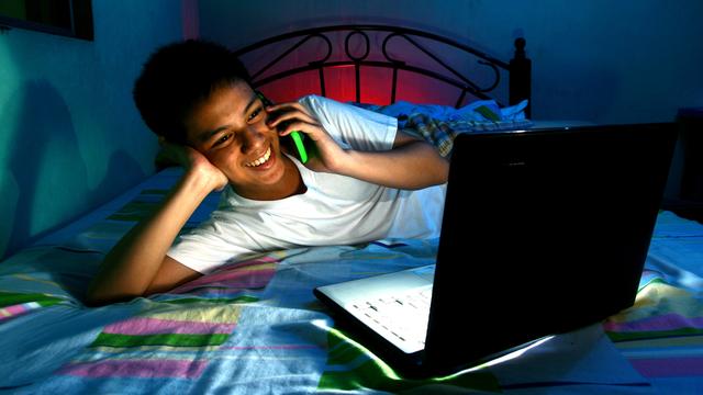 Un adolescent discute au téléphone tout en regardant son ordinateur. [Depositphotos - Junpinzon]