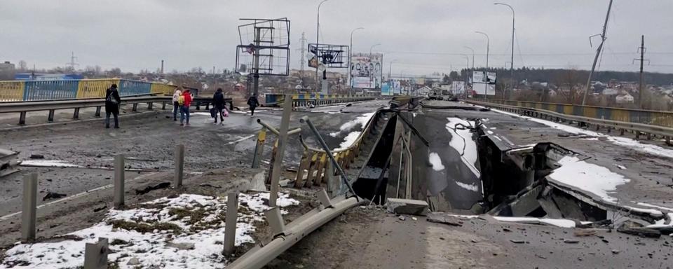 Des personnes marchent sur un pont détruit à Bucha, près de Kiev. [Reuters]