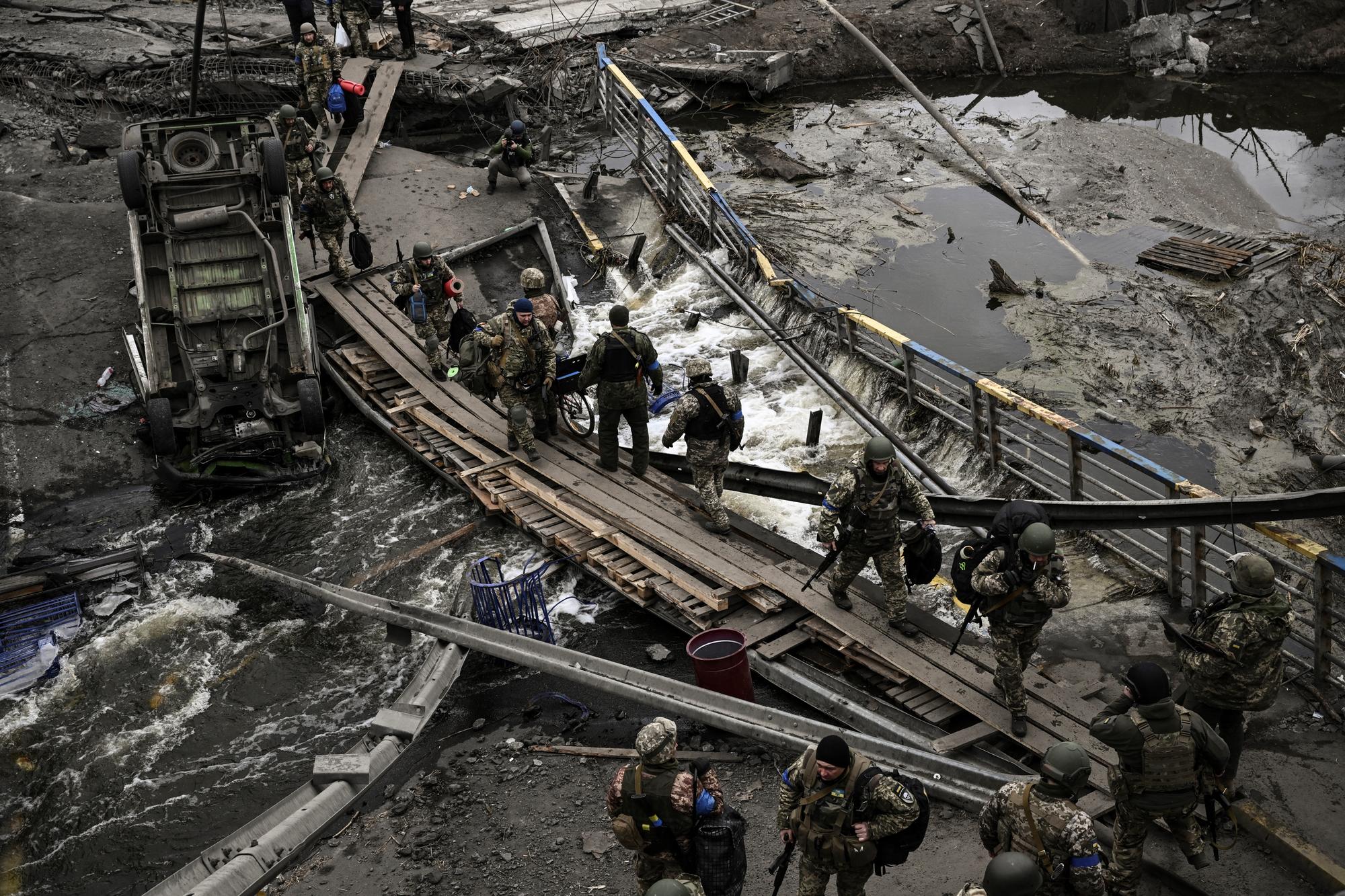 Des militaires ukrainiens marchent sur un chemin de fortune pour traverser une rivière à côté d'un pont détruit près de la ville d'Irpin, au nord-ouest de Kiev. [AFP - Aris Messinis]